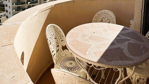 Un balcón con mesa y sillas, con vistas a un paisaje urbano con edificios altos y una masa de agua.