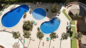 Amplia zona de piscina al aire libre con varias piscinas, tumbonas y palmeras.