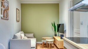 En moderne stue med sofa, et lille bord, et fjernsyn og et køkken med komfur.