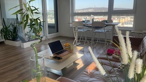 Un salon moderne avec un ordinateur portable posé sur une table, un canapé et de grandes fenêtres donnant sur la ville.