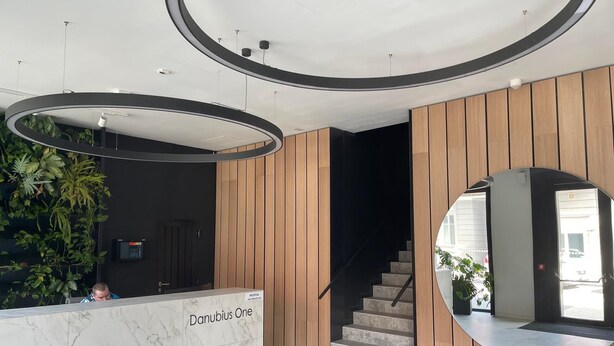 Un comptoir d’accueil portant l’inscription « Danubius One », au design moderne, un escalier et un miroir rond.