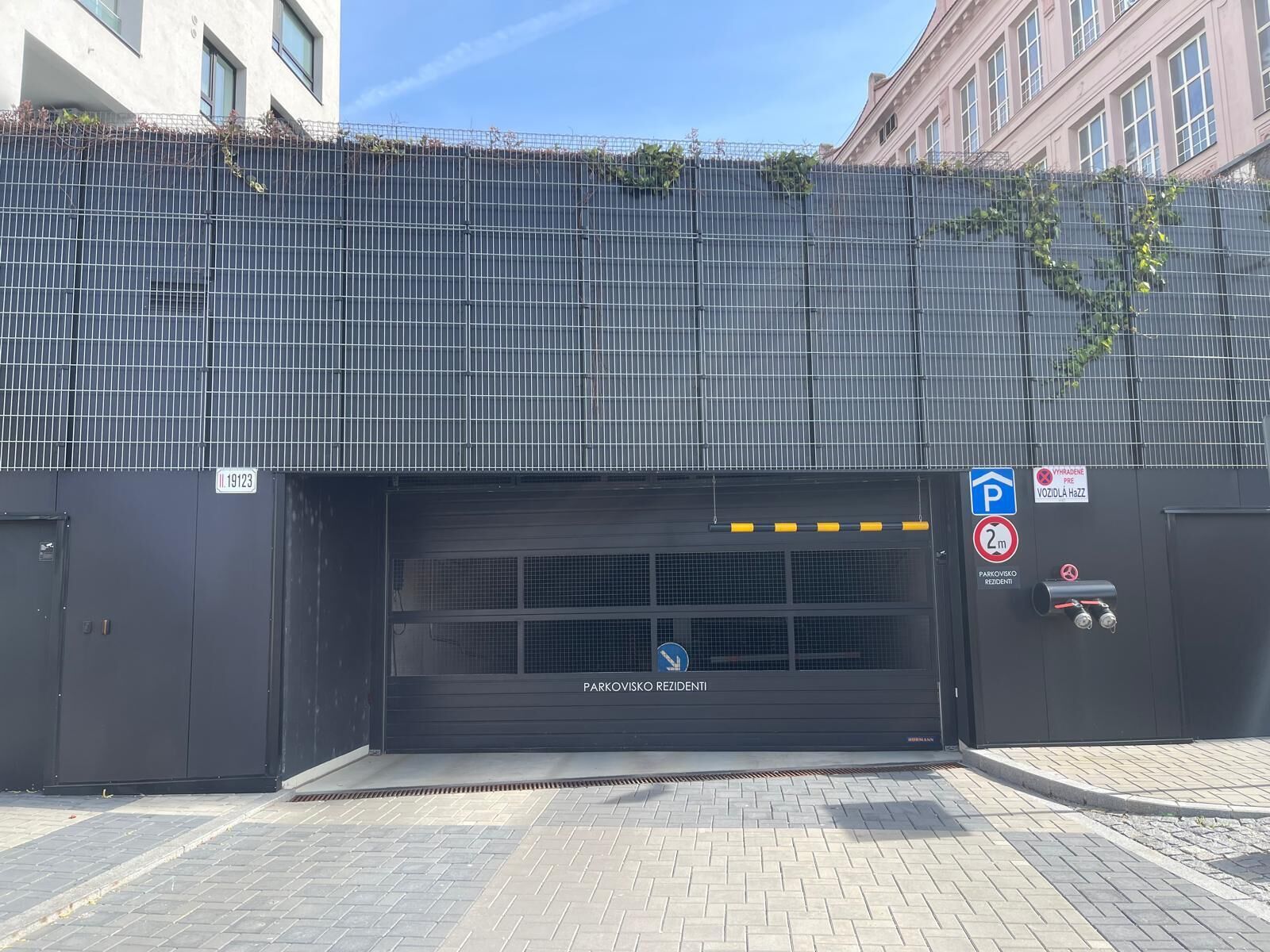 Ein verschlossener Eingang zu einem Wohnparkplatz mit einem Metallzaun, einem blauen Parkschild und einem Verbotsschild.
