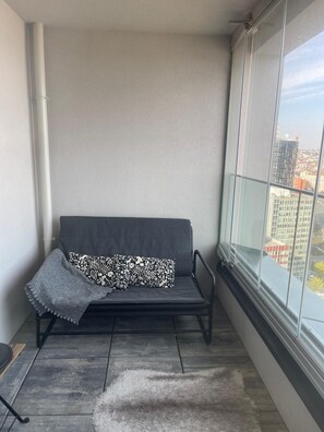 A corner balcony with a black sofa, a patterned throw pillow, and a fluffy rug.