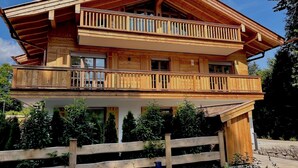 A two-story wooden chalet with a balcony on the upper floor, surrounded by greenery. - Bergliebe am Tegernsee: central, for 2, upscale, south-facing terrace, sauna, underground parking, near the lake (Rottach-Egern)