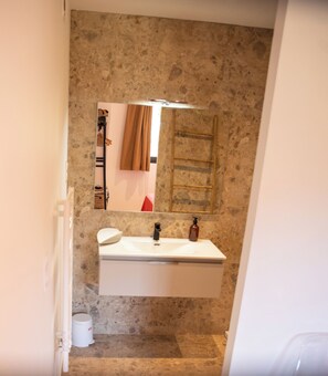 Ein Badezimmer mit Steinwand, Waschbecken in Weiß, Spiegel und Handtuchhalter.