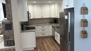 Una cocina moderna con armarios blancos, una pared de acento de piedra, un refrigerador empotrado y una chimenea de piedra.