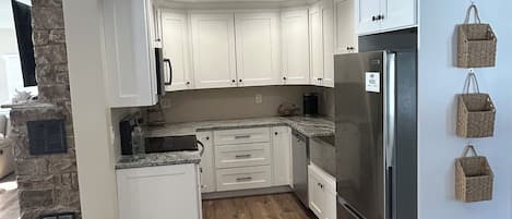 A modern kitchen with white cabinets, a stone accent wall, a built-in refrigerator, and a stone fireplace.