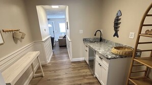 Una cocina con suelo de madera, armarios blancos, encimera de mármol y un adorno en forma de pez en la pared.