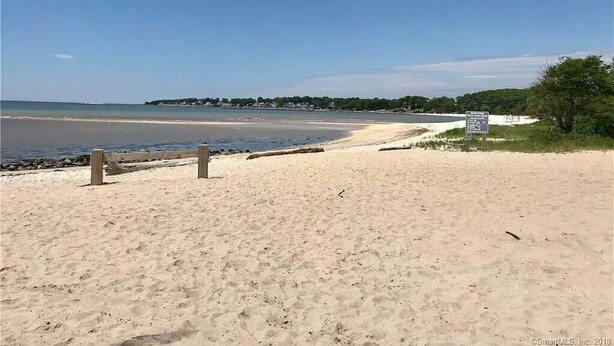 Una playa con una cerca de madera, un letrero y un cielo despejado.