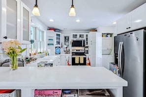 Una cocina moderna con armarios blancos, una isla grande, un refrigerador de acero inoxidable y un microondas.