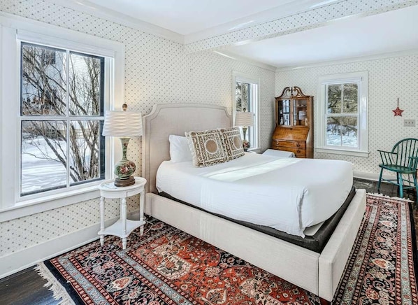 Un dormitorio con una cama grande, un armario de madera, una mesita de noche con una lámpara y una alfombra estampada.