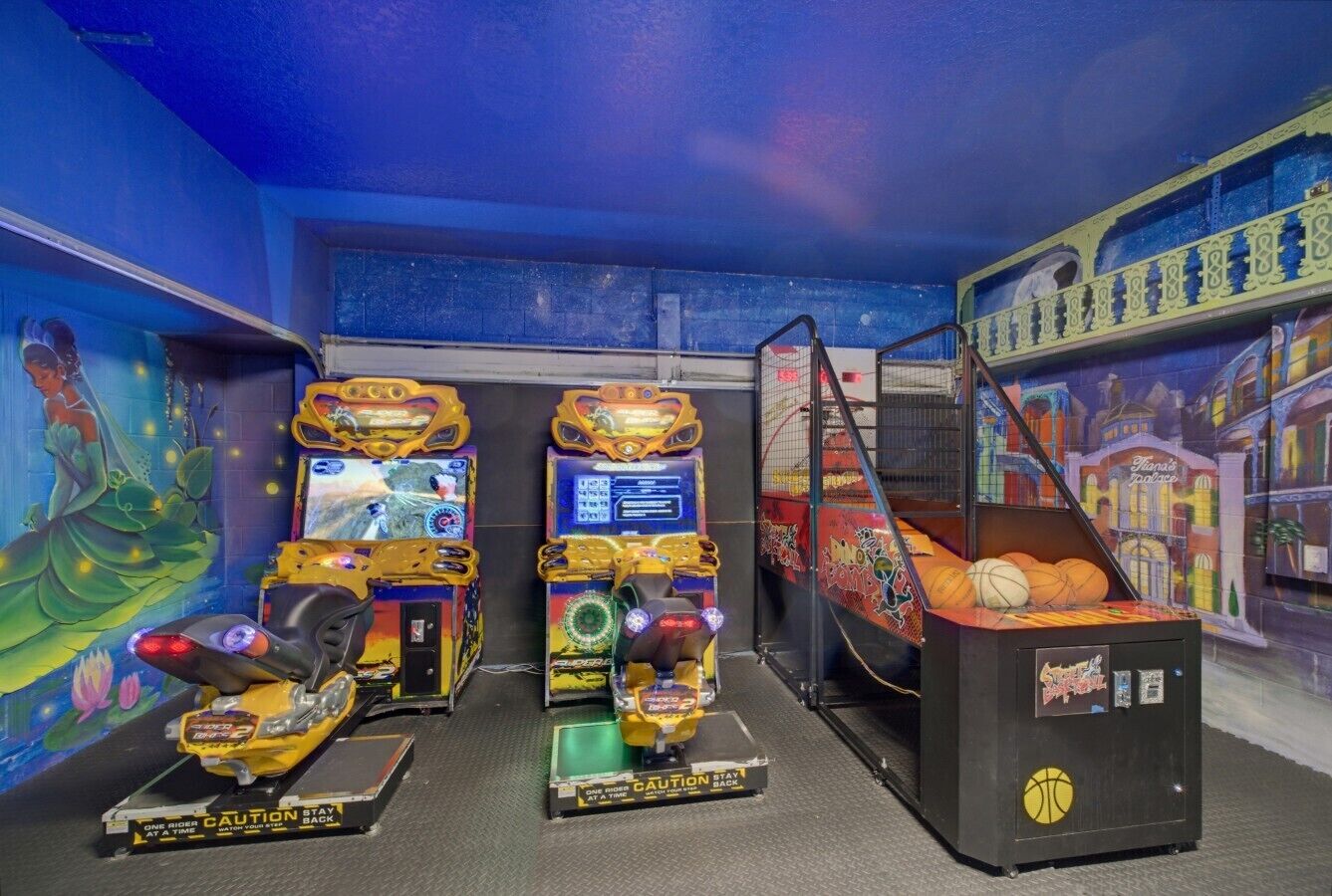 A room with arcade games, including a motorcycle game and a basketball game, and a mural on the wall.