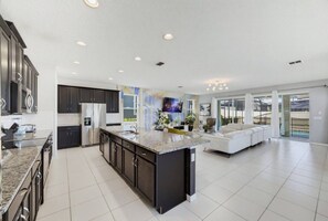 A modern kitchen with dark cabinetry, a large island, and a dining area with a white sofa. - 9BR The Sunset Paradise Resort w/ Pool Near Disney (Kissimmee)