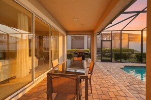 A modern outdoor patio with a pool, a dining area with a table and chairs, and a barbecue grill. - 9BR The Sunset Paradise Resort w/ Pool Near Disney (Kissimmee)