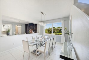 A modern dining area with a glass table, white chairs, and a view of greenery outside. - 9BR The Sunset Paradise Resort w/ Pool Near Disney (Kissimmee)
