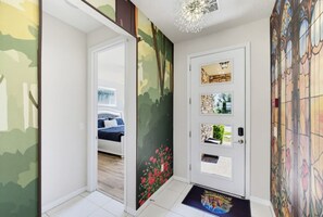 Ein Flur mit einer zurückliegenden Tür zu einem Schlafzimmer, einer Wand mit einem Wandgemälde zum Thema Natur und einem Buntglasfenster.