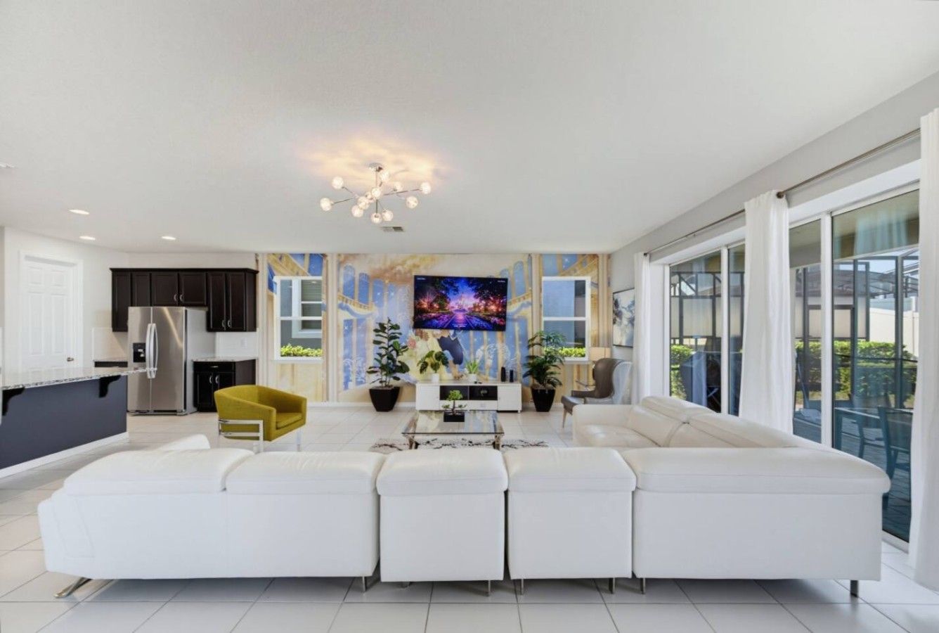 A modern living room with a white sectional sofa, a yellow chair, a flat-screen TV, and a dining area with a kitchen in the background.