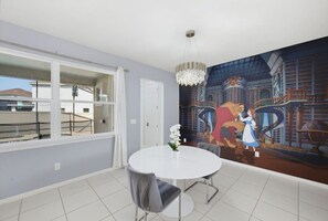 Ein Essbereich mit einem runden Tisch, Stühlen, einer Chandelüster und einem Wandgemälde.