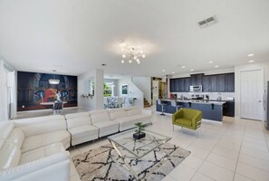 A modern living room with a white sofa, a glass coffee table, and a green armchair. - 9BR The Sunset Paradise Resort w/ Pool Near Disney (Kissimmee)