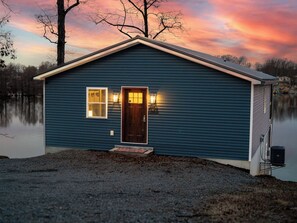 A small, single-story building with a dark blue exterior, a front door, and two windows with exterior lighting. - Blue Blessing, Hot tub, Waterfront, bunk room (Goreville)