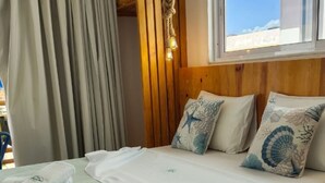 Habitación de hotel con dos camas, un cabecero de madera, una ventana con vistas y una cortina.