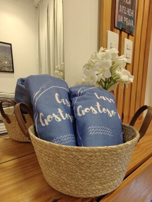 Un panier tressé contenant deux coussins bleus, chacun orné du mot « Gostoso », est posé sur une table en bois.