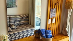 Habitación de hotel con un espejo grande, un sofá a rayas, una mesa consola de madera con cestas y vista al mar por la ventana.