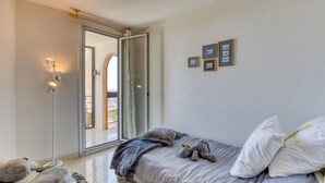 Ein Schlafzimmer mit einem Bett, Kissen, einem Teddybär, einer Stehlampe und einer Glastür, die auf einen Balkon führt.