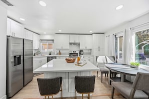Une cuisine moderne avec des meubles blancs, un îlot central et un coin repas avec des chaises.