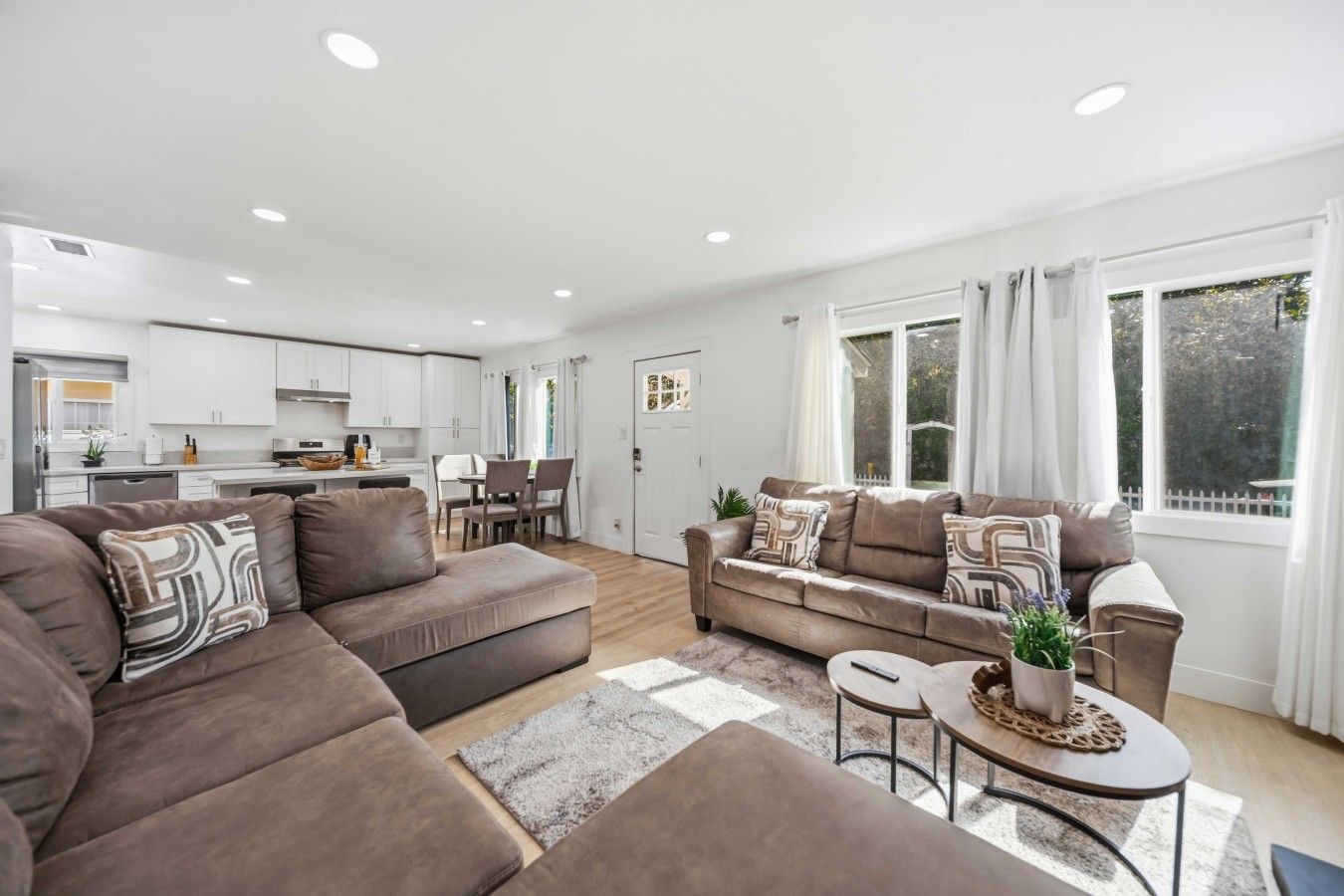 A modern living room with a sofa set, a dining area, and a kitchen in the background.