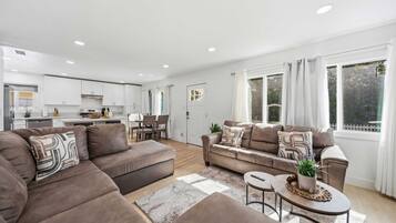 A modern living room with a sofa set, a dining area, and a kitchen in the background.