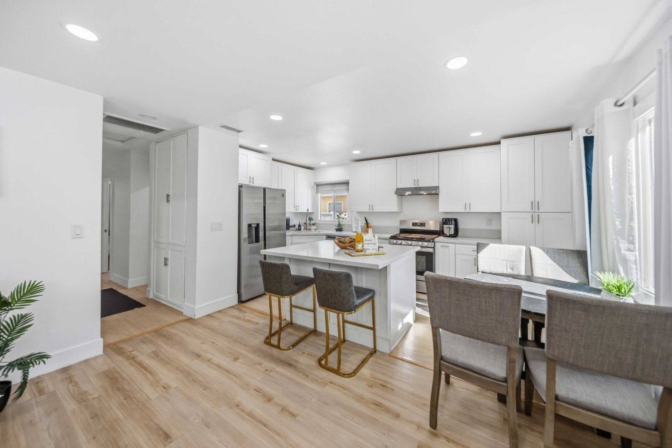 A modern kitchen with white cabinets, a central island with bar stools, and a dining area with a table and chairs.