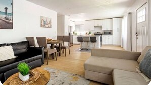 Una sala de estar moderna con un sofá de cuero negro, un sofá color beige y un comedor con mesa y sillas.