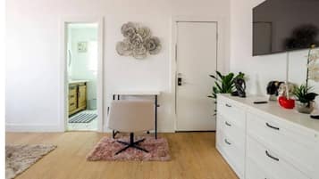 Een moderne kamer met een wit bureau, een stoel, een grote spiegel en een witte ladekast.