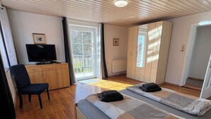 A room with a wooden ceiling, a bed with a grey and beige duvet, a TV on a wooden cabinet, and a chair. - Vacation apartment Oberland Ammersee Landsberg (Pürgen)
