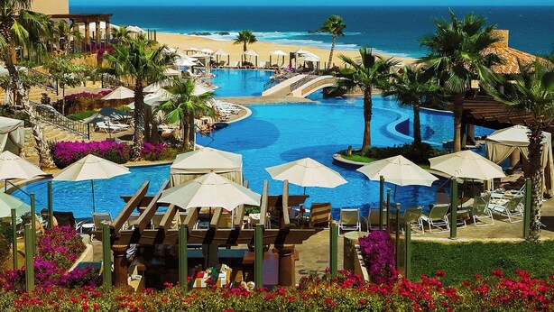 A resort pool area with a view of the ocean, surrounded by palm trees and lounge chairs. - GORGEOUS 3-bedroom villa in Cabo San Lucas - infinity pool (Cabo San Lucas)
