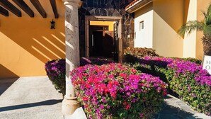 A building entrance with a stone archway, a door, and vibrant flower beds. - GORGEOUS 3-bedroom villa in Cabo San Lucas - infinity pool (Cabo San Lucas)