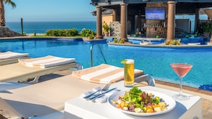 A poolside dining area with a table set for a meal, a tall glass of beer, and a martini glass. - GORGEOUS 3-bedroom villa in Cabo San Lucas - infinity pool (Cabo San Lucas)