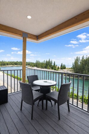 En overdækket terrasse med et rundt bord og fire stole, med udsigt over vand og skov.