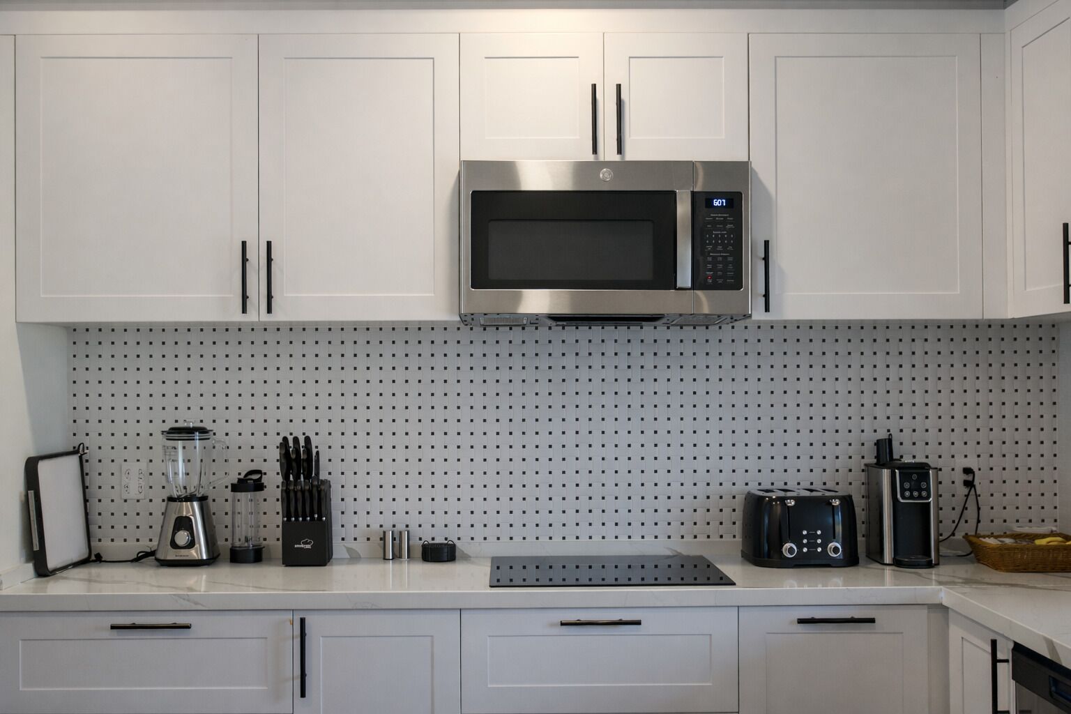 Una cocina con armarios blancos, un microondas de acero inoxidable, un tostador y una cafetera.