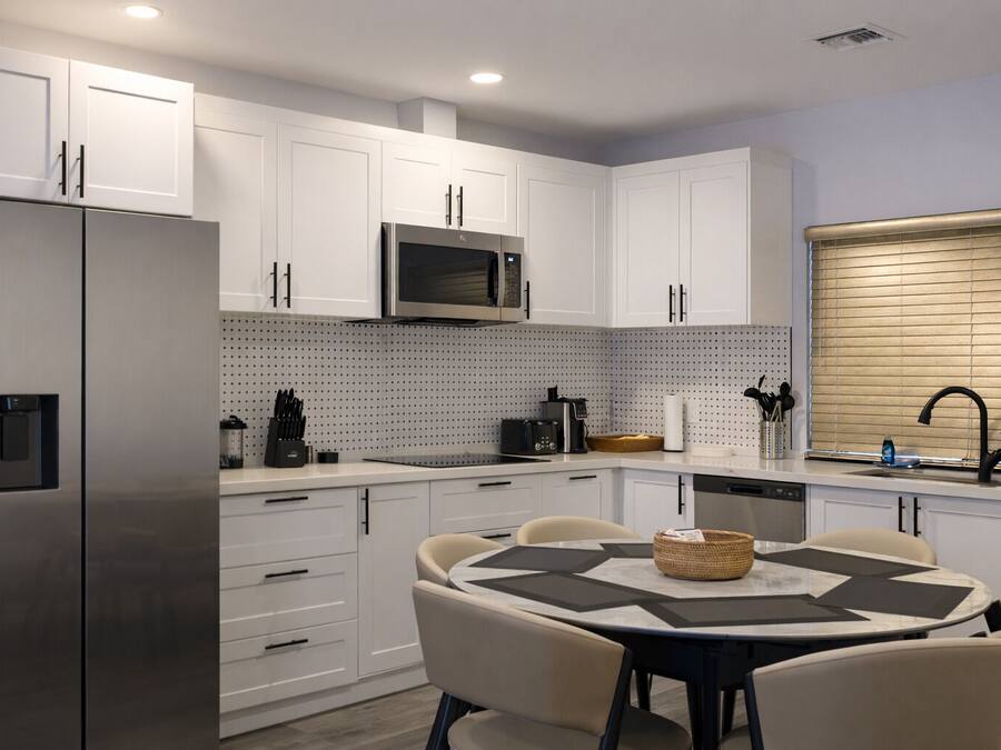 A modern kitchen with white cabinets, a stainless steel refrigerator, a microwave, and a dining area with a round table and chairs.
