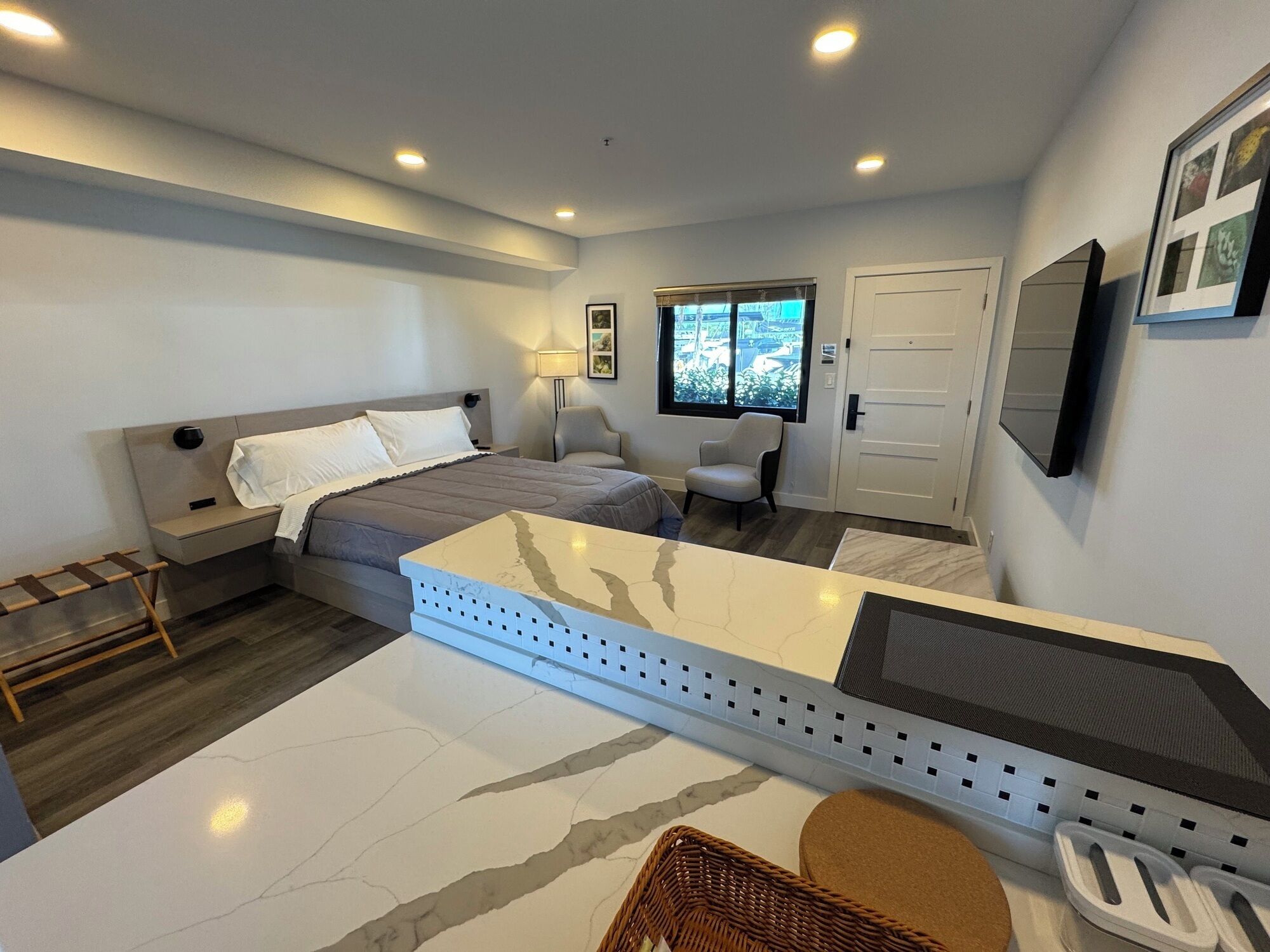 Un dormitorio moderno con cama, mesitas de noche, una silla, un escritorio, una ventana y una puerta.