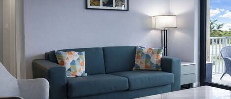 A modern living room with a sofa, two patterned pillows, a side table, a floor lamp, and a framed picture on the wall.