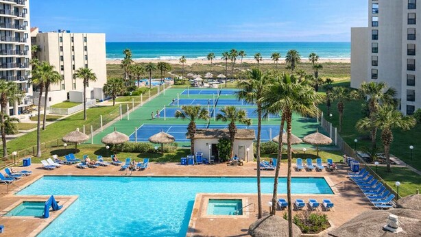 Een hotel met een zwembad, tennisbanen en uitzicht op het strand.