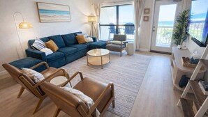 Een woonkamer met een bank, twee fauteuils, een salontafel, een televisie en een balkon met uitzicht.