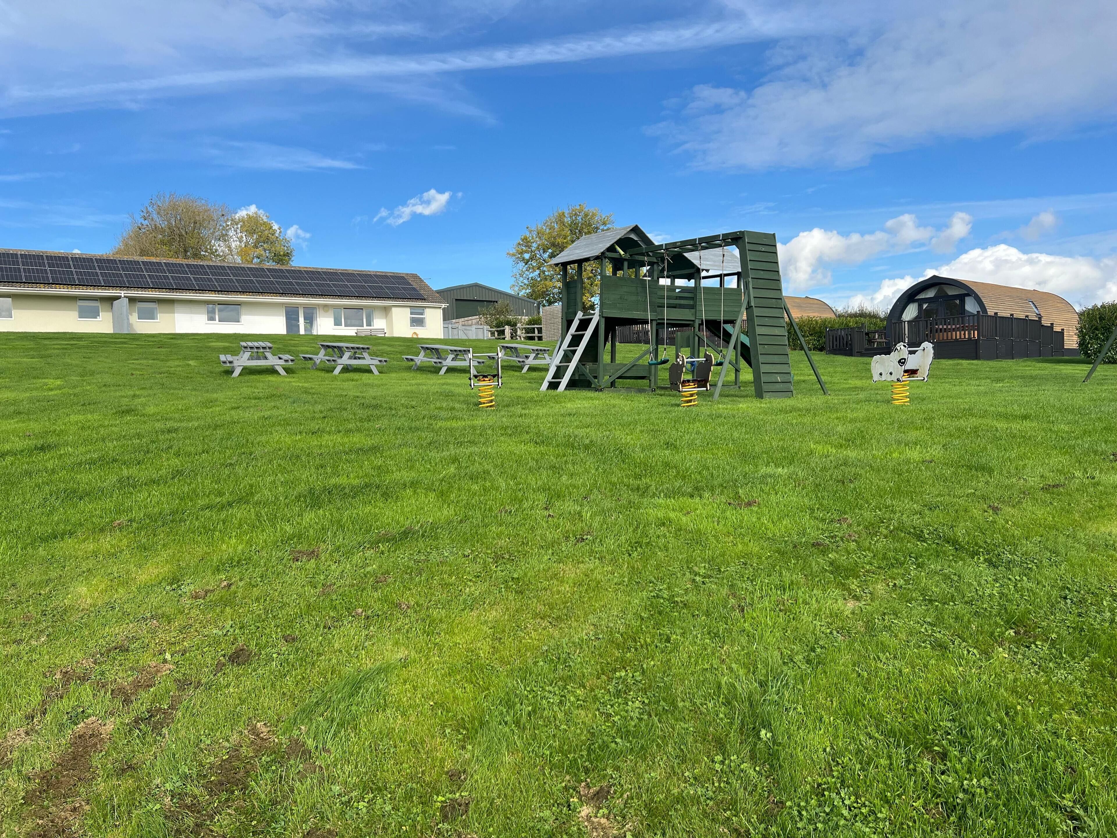 A playground with swings and slides, picnic tables, and a green climbing structure.