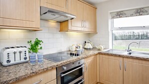 Una cucina moderna con mobili in legno, forno incassato, cappa aspirante in acciaio inossidabile, piano di lavoro in granito e una finestra vista alberi.