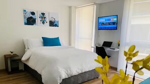 A modern hotel room with a large bed, a desk with a laptop, and a TV on the wall. - Lovely loft downtown - La Candelaria (Bogotá)