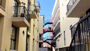 Un étroit passage piétonnier entre des immeubles à plusieurs étages dotés de balcons, avec un escalier central et des plantes en pot disposées le long des murs.