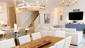 A modern dining area with a wooden table, white upholstered chairs, and a chandelier.